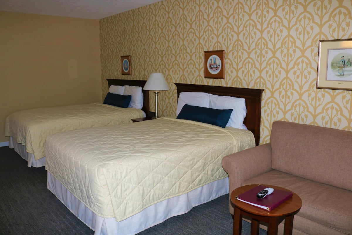 A hotel room with two beds, a sofa, a small table, and a lamp.