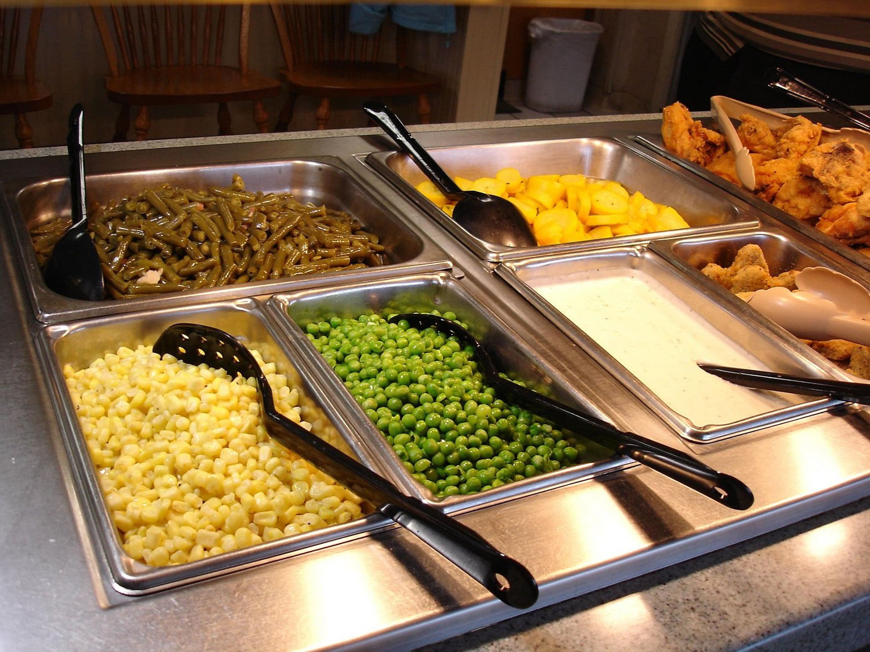A buffet with various food options including corn, peas, green beans, potatoes, and fried items.