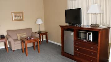 A hotel room with a beige sofa, a wooden coffee table, a television, a microwave, a lamp, and a telephone.