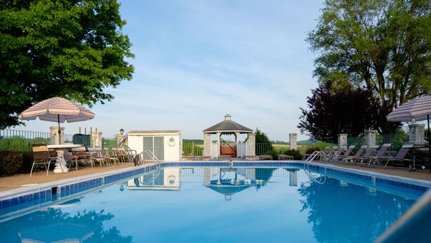A swimming pool with lounge chairs and umbrellas, a gazebo, and a small building with a window.