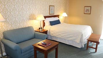 Een hotelkamer met een bed, een slaapbank, een nachtkastje met een lamp en een klein houten bankje.