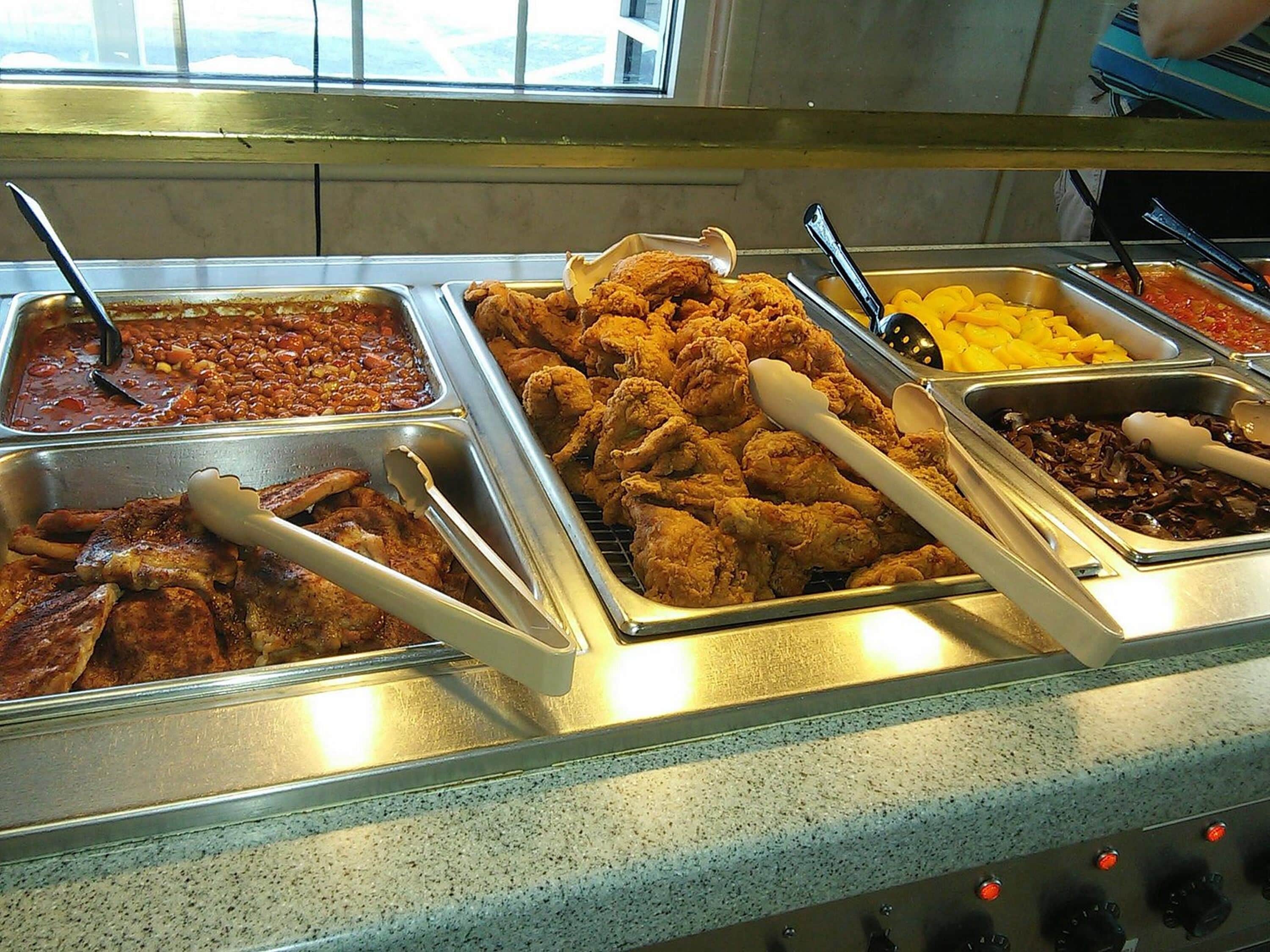 Un bufé con diversos platos, incluyendo pollo frito, frijoles y verduras.