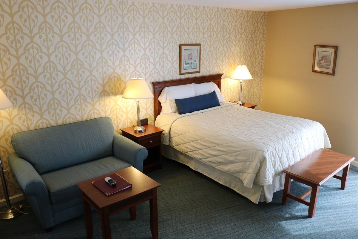 A hotel room with a bed, a sofa, a nightstand, a table, and two lamps.