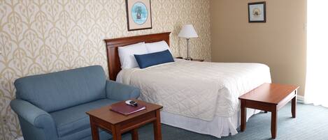 A hotel room with a bed, a blue sofa, a wooden nightstand, and a lamp.
