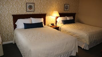 Duas camas de solteiro com roupa de cama branca e azul, uma mesa de cabeceira com abajur e papel de parede estampado.
