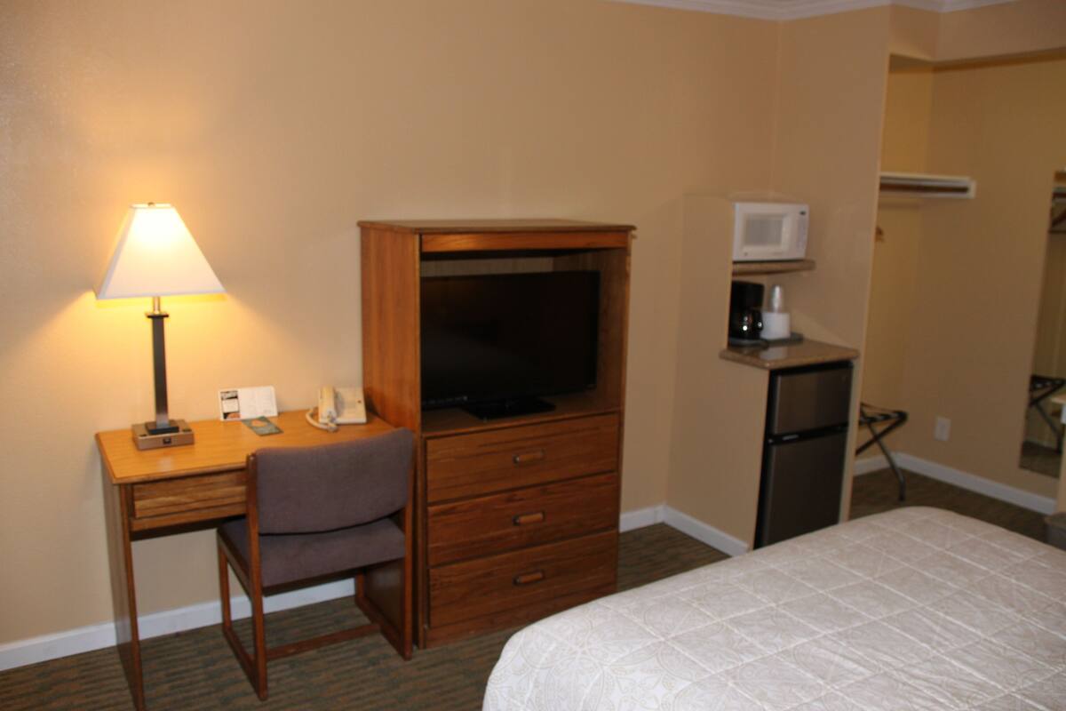 A hotel room with a wooden desk, a television, a refrigerator, and a bed.
