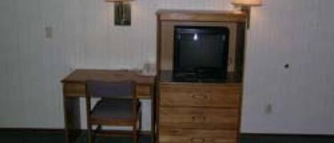 Een kleine kamer met een houten bureau, een stoel, een televisie op een houten kast en twee wandlampen.