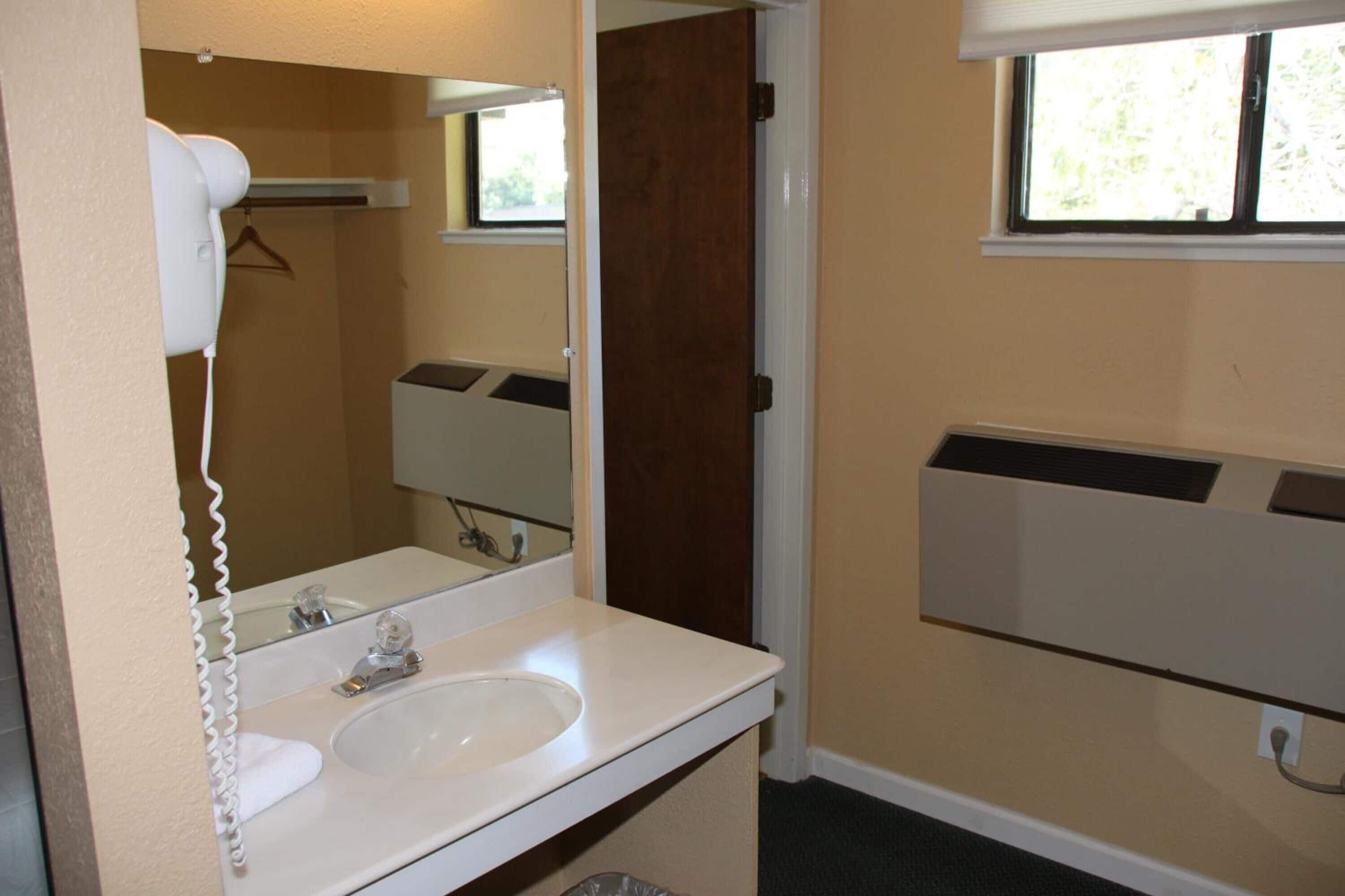 A bathroom with a white sink, a mirror, a towel rack, and a window.