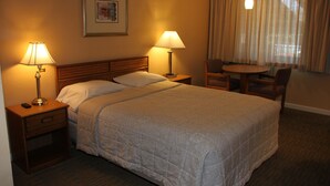 A hotel room with a large bed, two bedside tables with lamps, a small table with chairs, and a window with curtains.