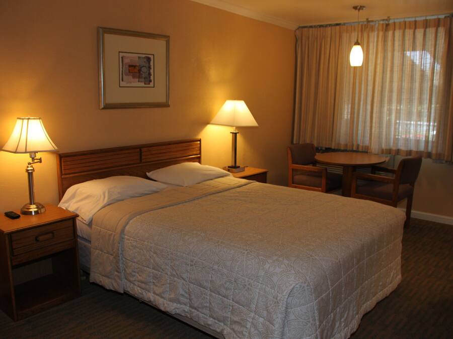 A hotel room with a large bed, two bedside tables with lamps, a small table with chairs, and a window with curtains.