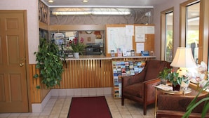 A reception area with a wooden reception desk, a red carpet, a comfortable armchair, and a potted plant.