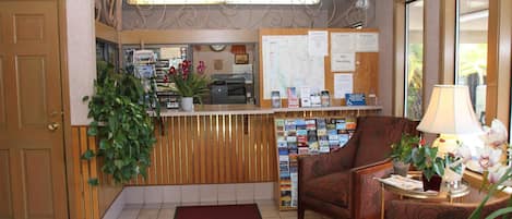 A reception area with a wooden reception desk, a red carpet, a comfortable armchair, and a potted plant.
