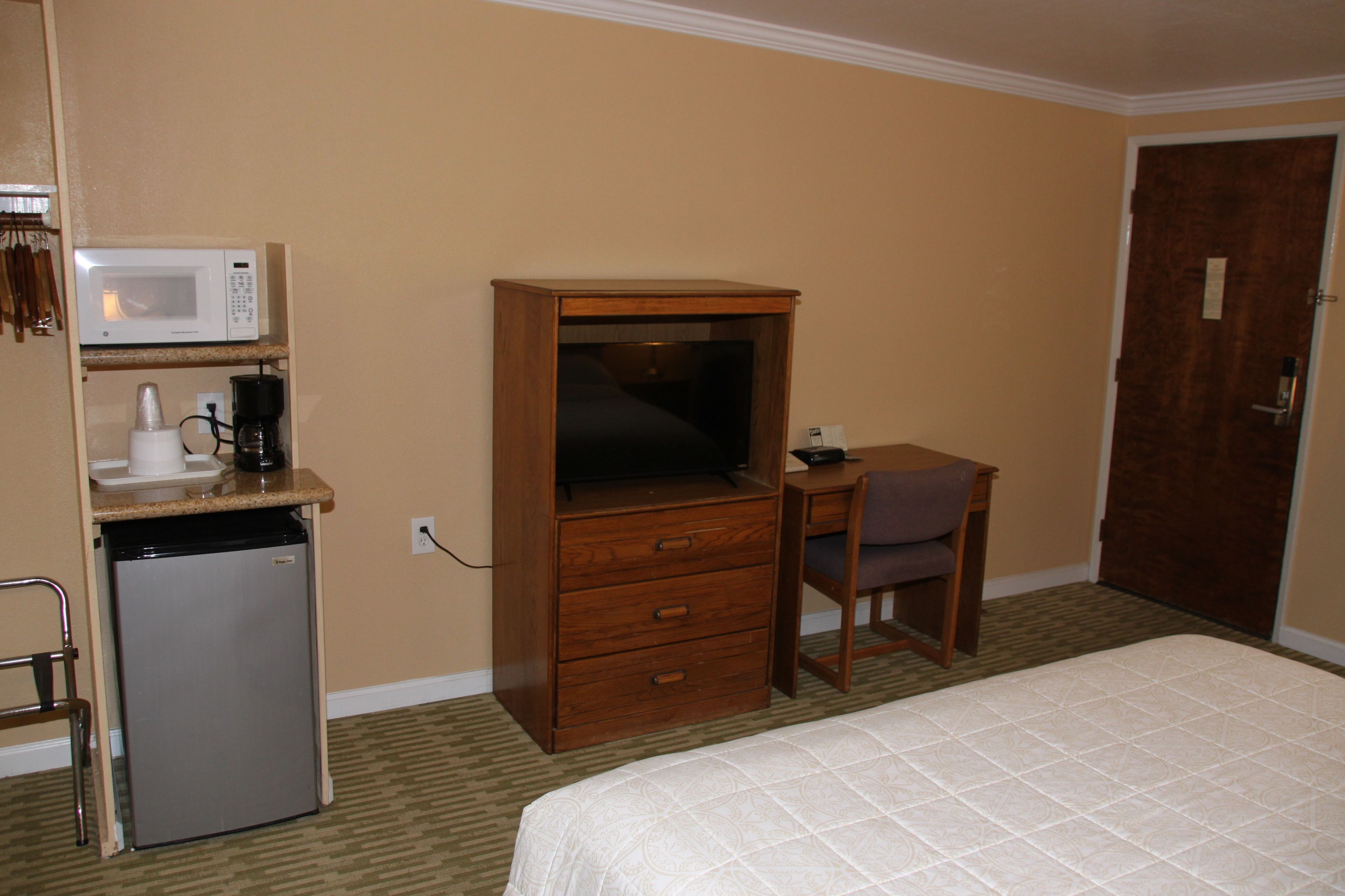 A hotel room with a bed, a wooden desk, a television, a microwave, and a refrigerator.