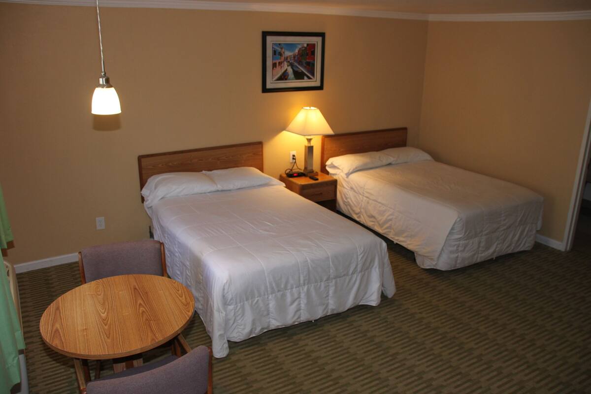 A hotel room with two beds, a wooden table, and a lamp.