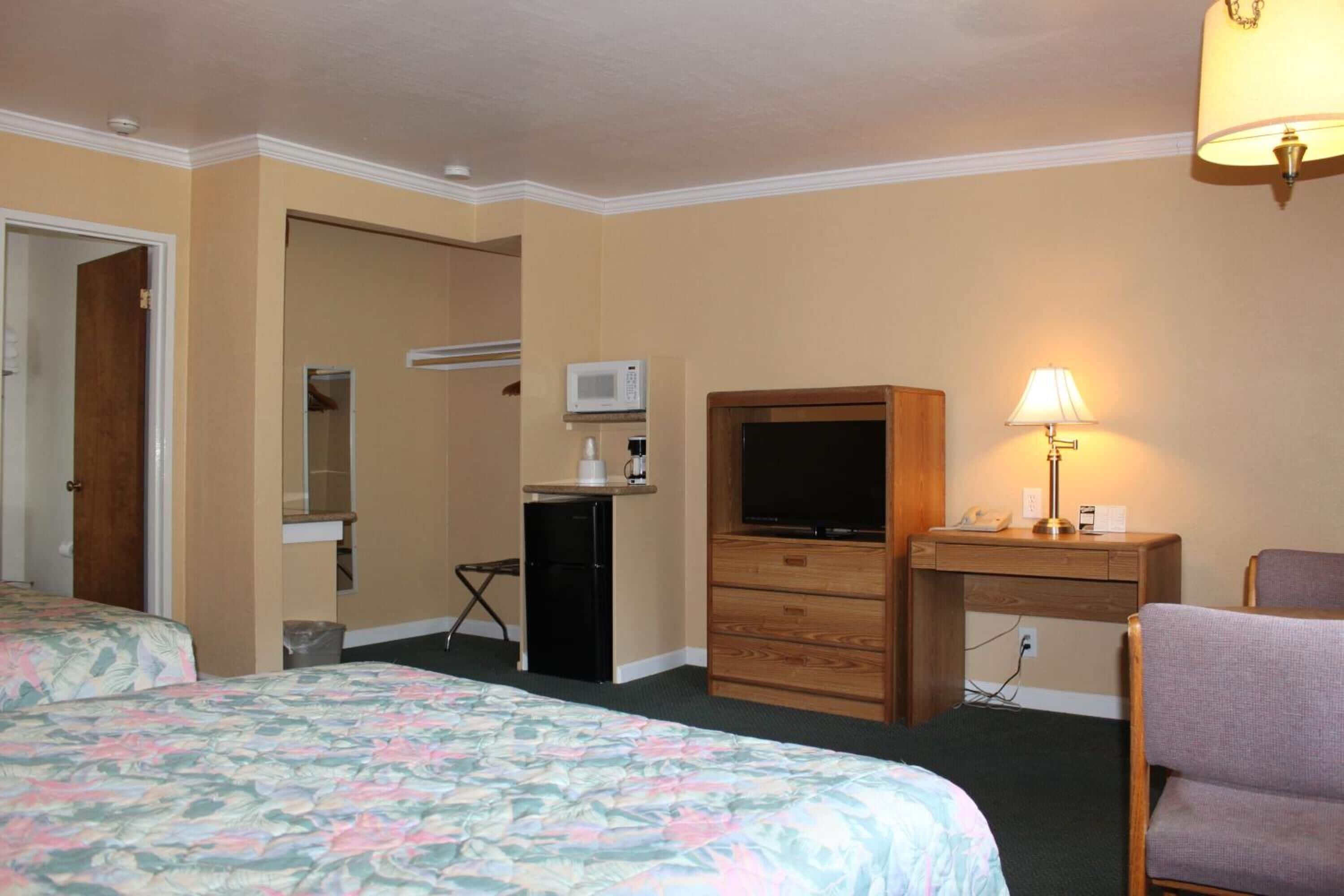 Habitación de hotel con dos camas, televisión, escritorio con lámpara, microondas y refrigerador pequeño.