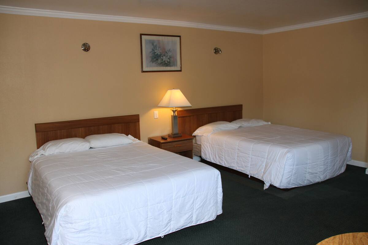 A hotel room with two single beds, a nightstand with a lamp, and a framed picture on the wall.