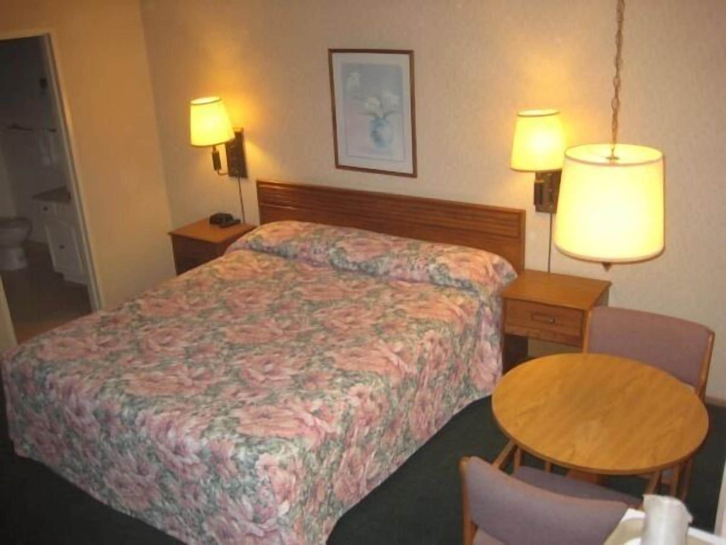 Une chambre d’hôtel comprenant un lit, une table de chevet, une chaise et deux lampes fixées au mur.
