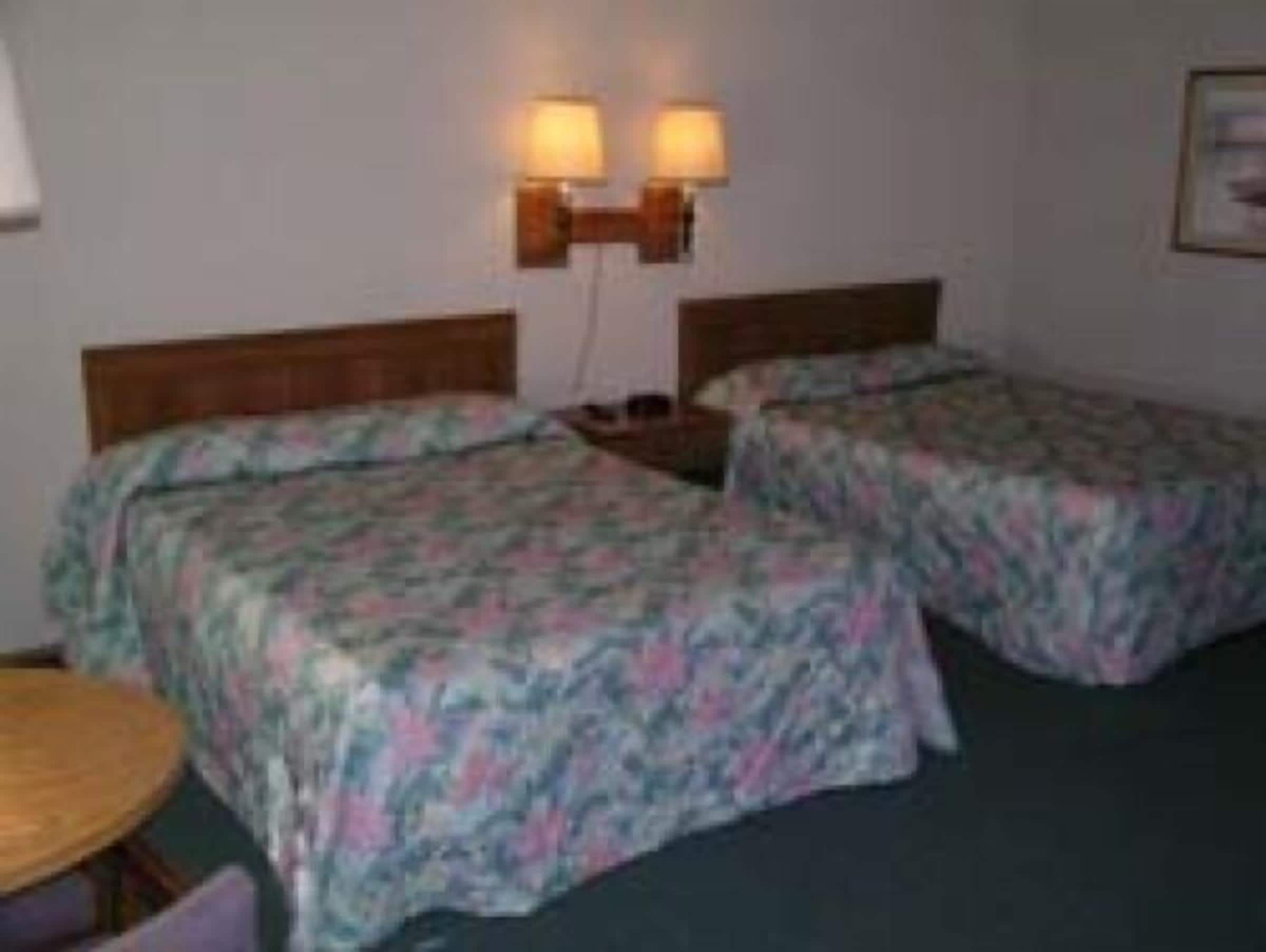 A room with two beds, a small table, and two wall-mounted lamps.