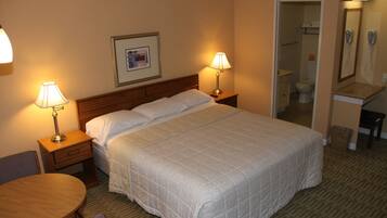 A hotel room with a large bed, two bedside tables with lamps, a small round table, and a chair. There is a framed picture on the wall above the bed.
