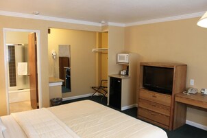 A hotel room with a bed, a desk with a television, a microwave, and a telephone.
