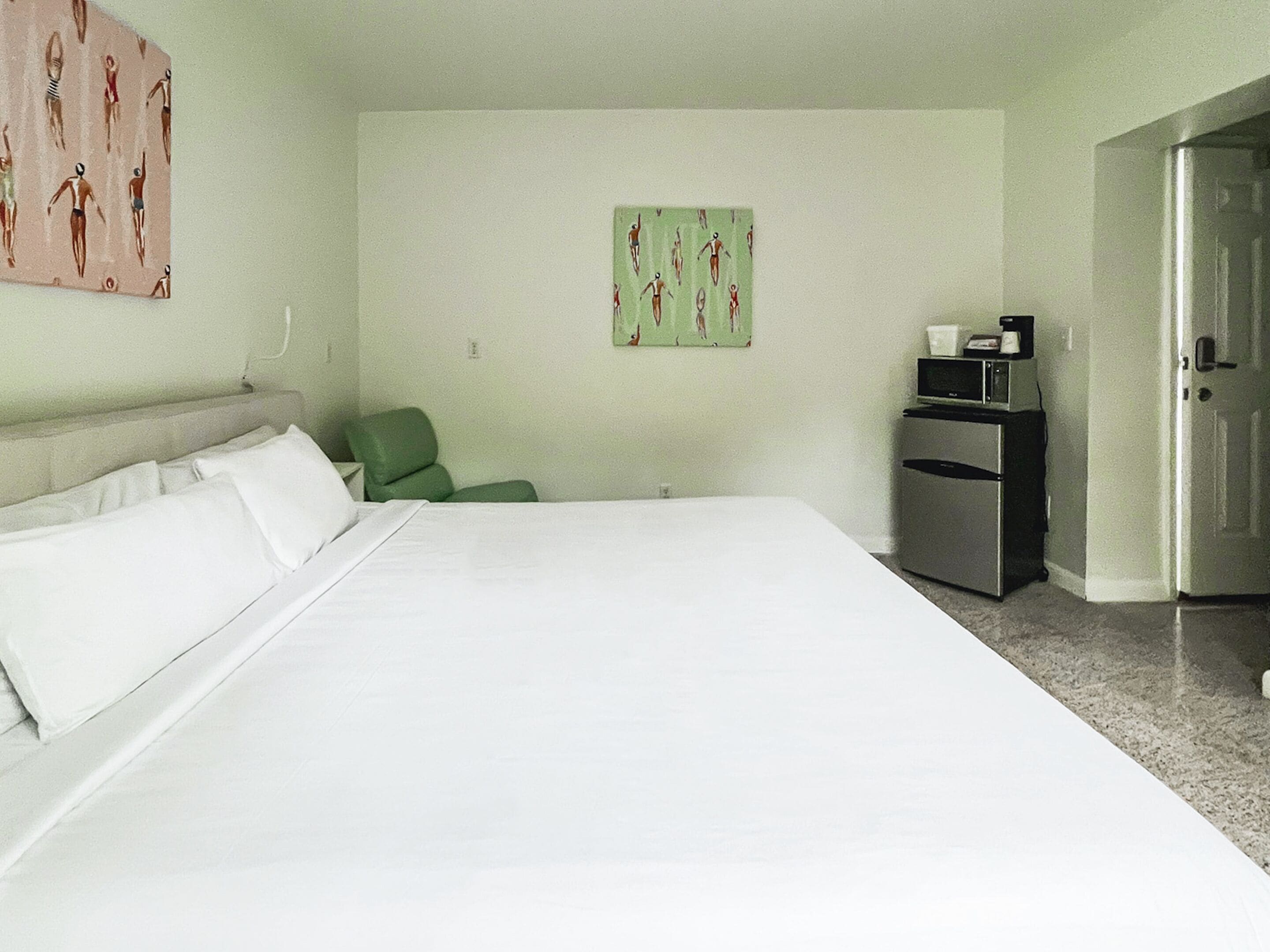 A hotel room with a large bed, a green chair, a microwave, and a refrigerator.