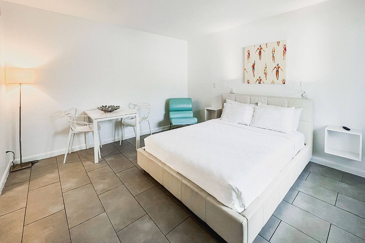 Una habitación de hotel moderna con una cama grande, un escritorio con sillas, una lámpara y una obra de arte en la pared.