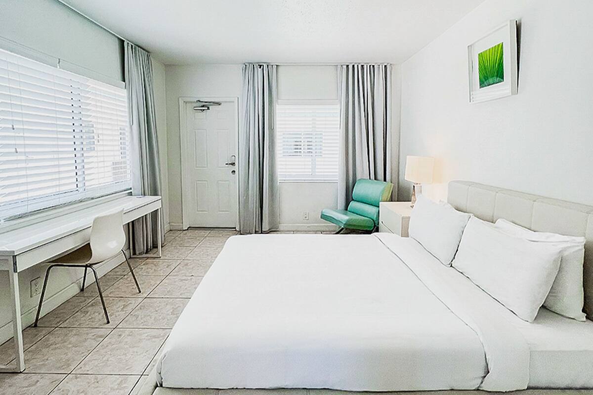Habitación de hotel con una cama grande, un escritorio, una silla y una ventana con persianas.