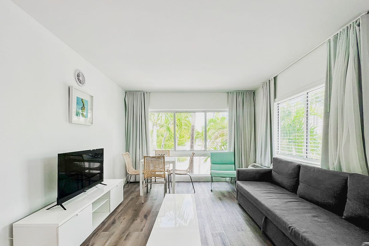 Una sala de estar moderna con un televisor de pantalla plana, un sofá, una mesa de centro y una zona de comedor con sillas.