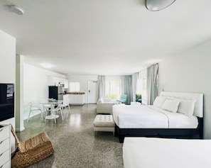 A modern hotel room with a large bed, a separate seating area with a table and chairs, a kitchenette, and a view of the outdoors. - Tranquilo A North Beach Village Resort Hotel (Fort Lauderdale)