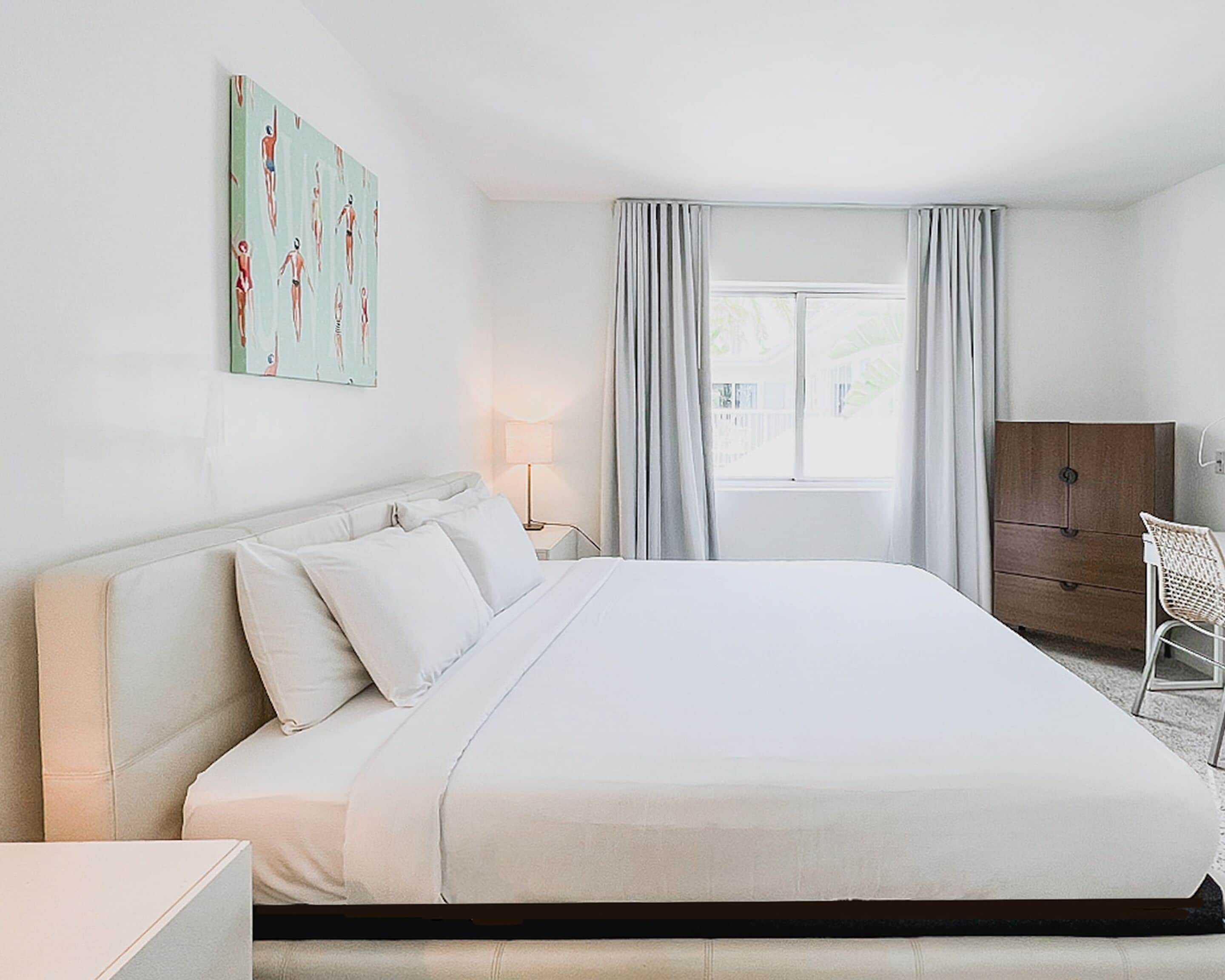 Een hotelkamer met een groot bed, een nachtkastje met een lamp, een kledingkast en een raam met gordijnen.