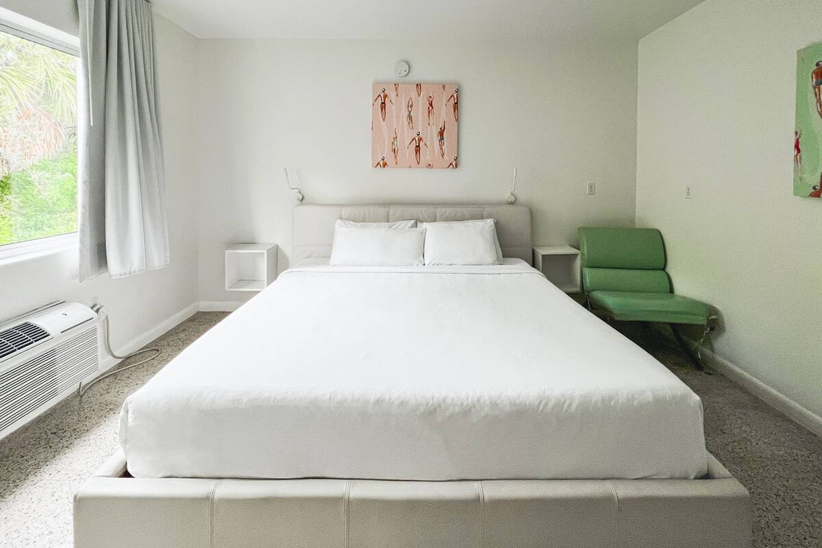 Un dormitorio con una cama grande, una silla verde y una ventana con cortinas.