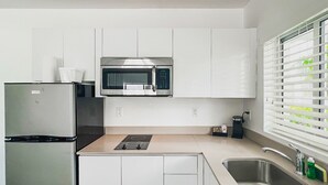 Una cocina moderna con armarios blancos, un refrigerador de acero inoxidable, un microondas y un lavamanos.