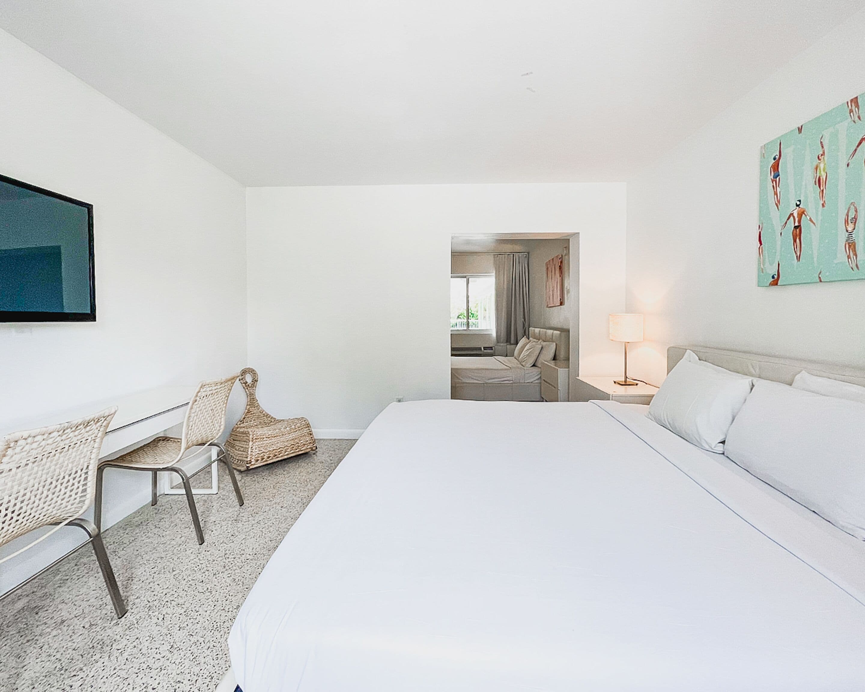 A hotel room with a large bed, a desk with a chair, a lamp, and a painting on the wall.