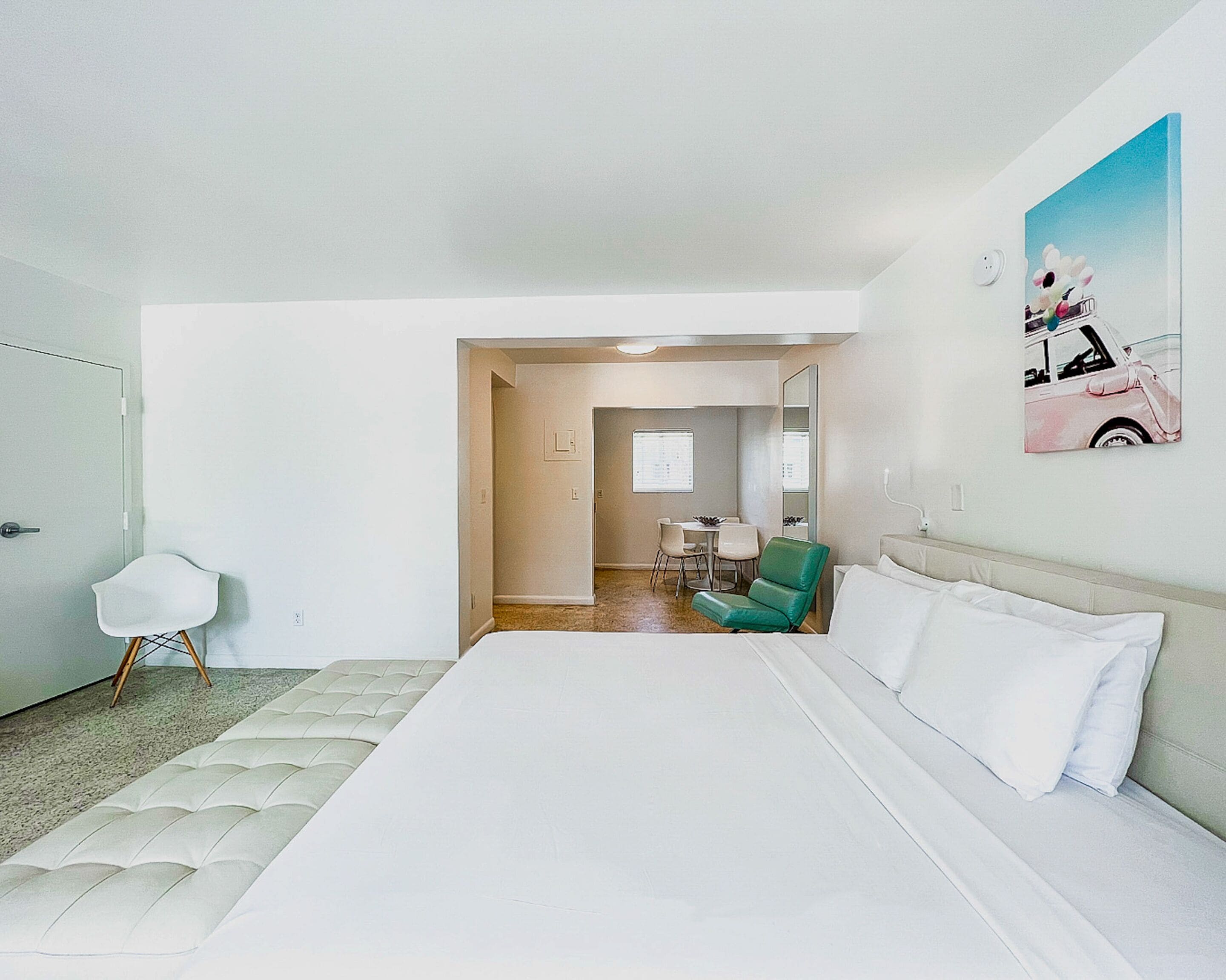 Ein Hotelzimmer mit einem großen Bett, einem grünen Sessel, einem weißen Schreibtisch und einem Essbereich im Hintergrund.