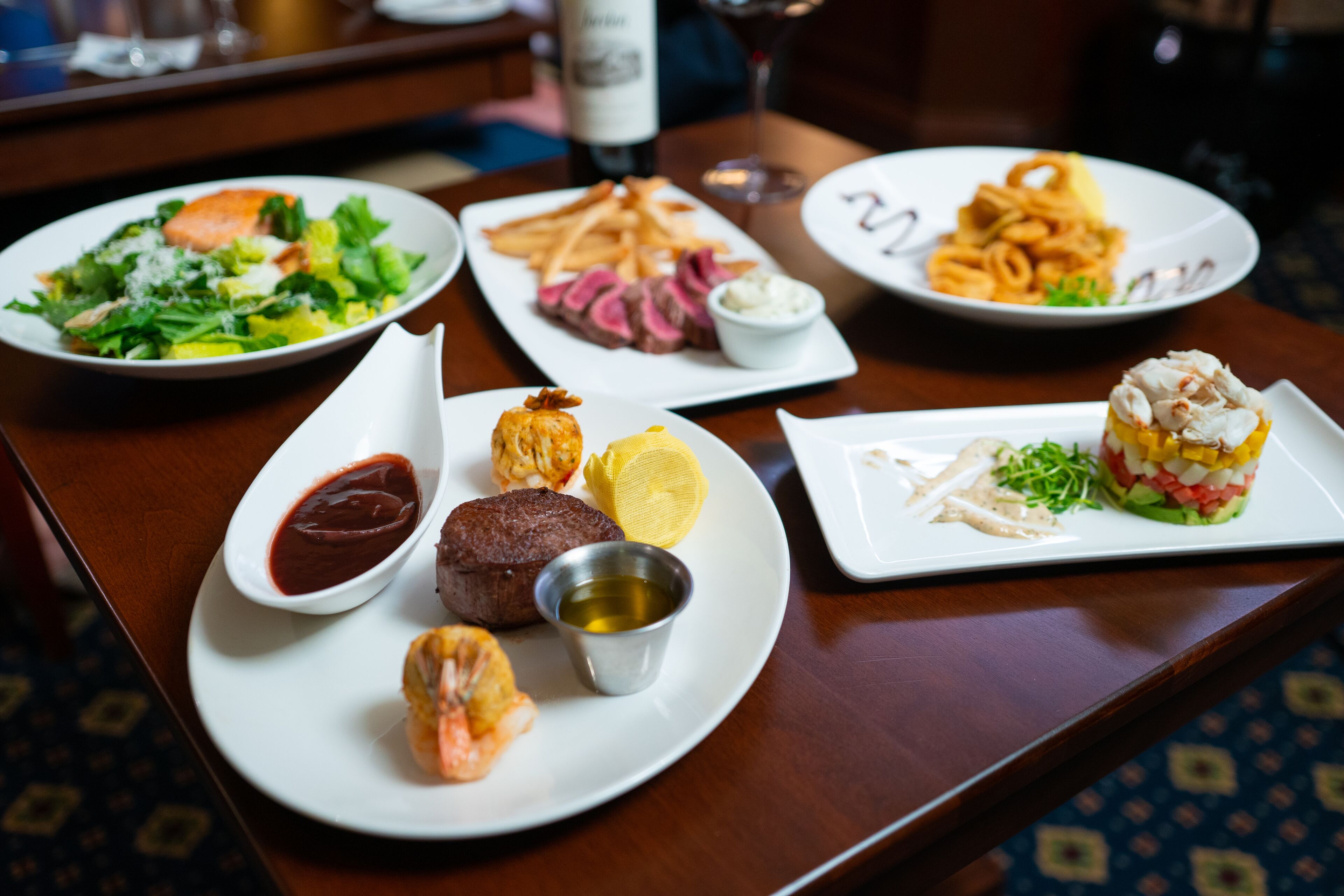 A dining table with various plates of food, including salads, steak, and seafood.