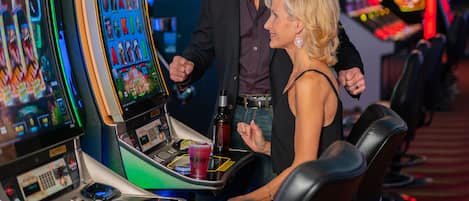 Un casino con máquinas tragamonedas y un hombre y una mujer de pie junto a una de ellas.