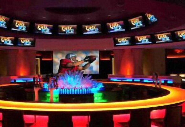 A bar area with multiple screens displaying content, a central bar counter, and a person in a red uniform. - Bally's Dover Casino Resort (Dover)