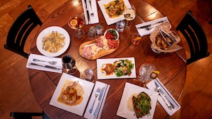 A round wooden table with four plates of food, cutlery, and glasses.