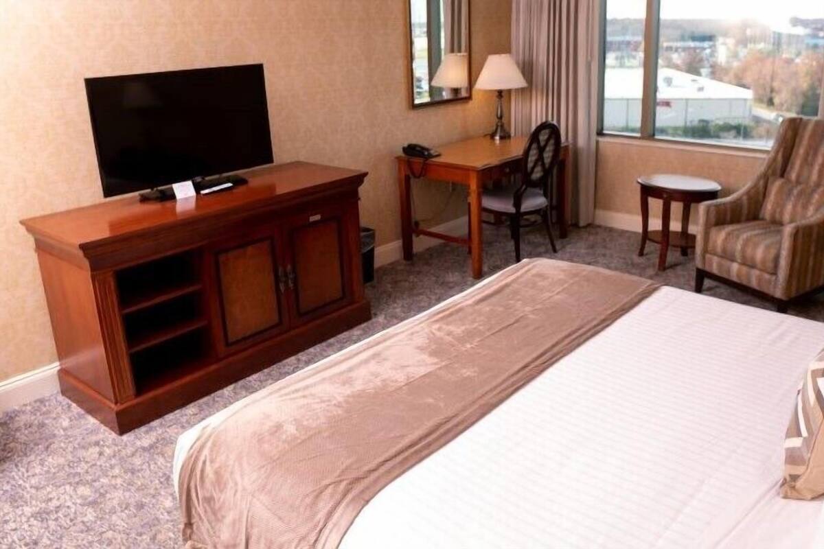 Habitación de hotel con cama, televisor, escritorio con silla y ventana con cortinas.