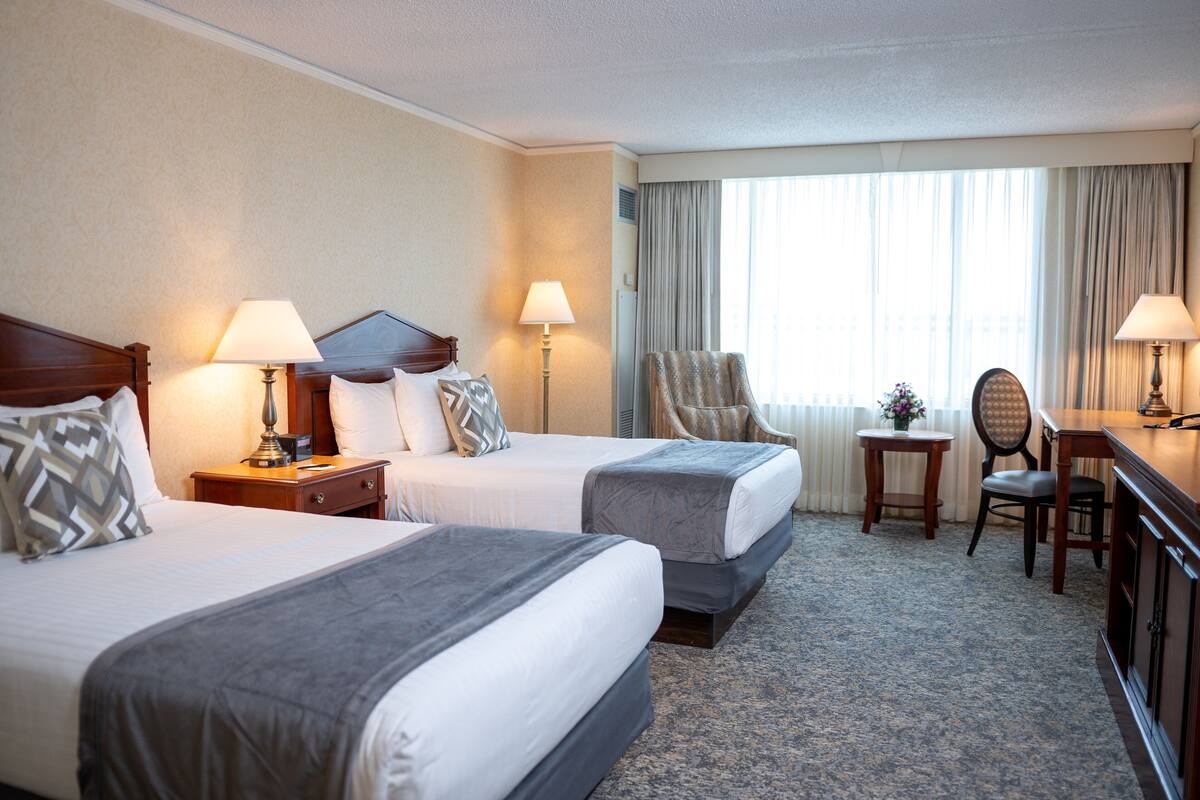 Habitación de hotel con dos camas, un escritorio, una silla y una lámpara.
