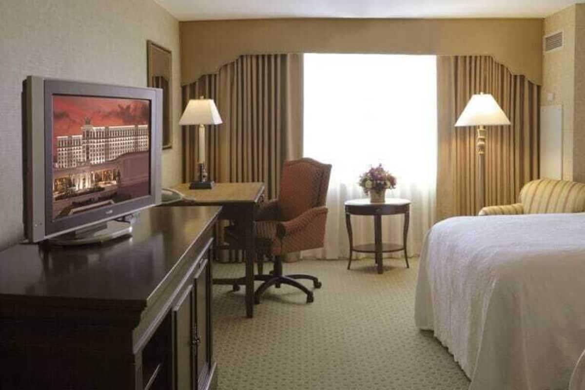 Habitación de hotel con dos camas, un escritorio con televisor, una silla y una mesita con lámpara.