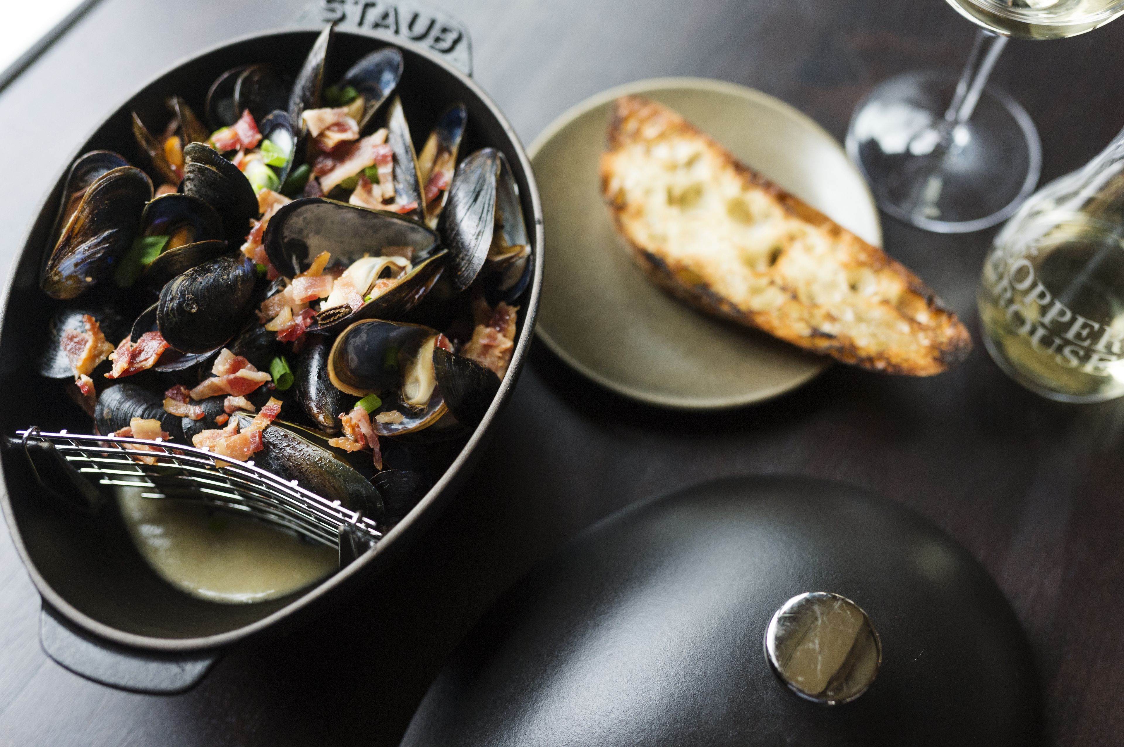 Prato de frutos do mar com mexilhões, bacon e vegetais verdes numa tigela preta.