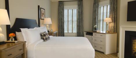 A hotel room with a large bed, a desk, a chair, a fireplace, and a window with curtains.