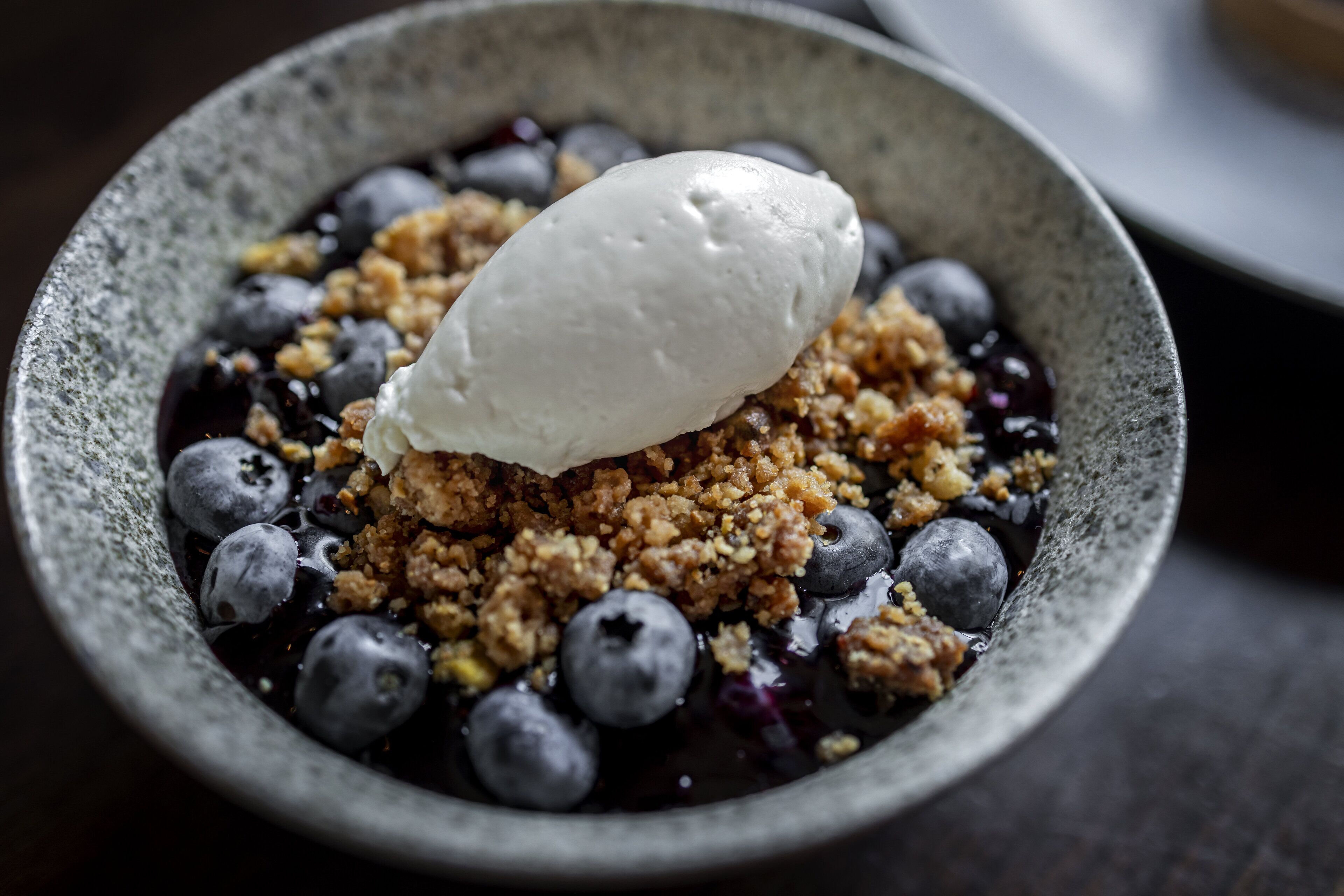 Un bol de dessert composé de myrtilles, d’une garniture émiettée et d’une boule de crème glacée.