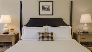 A neatly made bed with a checkered pillow, two bedside tables with lamps, a framed picture on the wall, and a small clock on one of the tables.