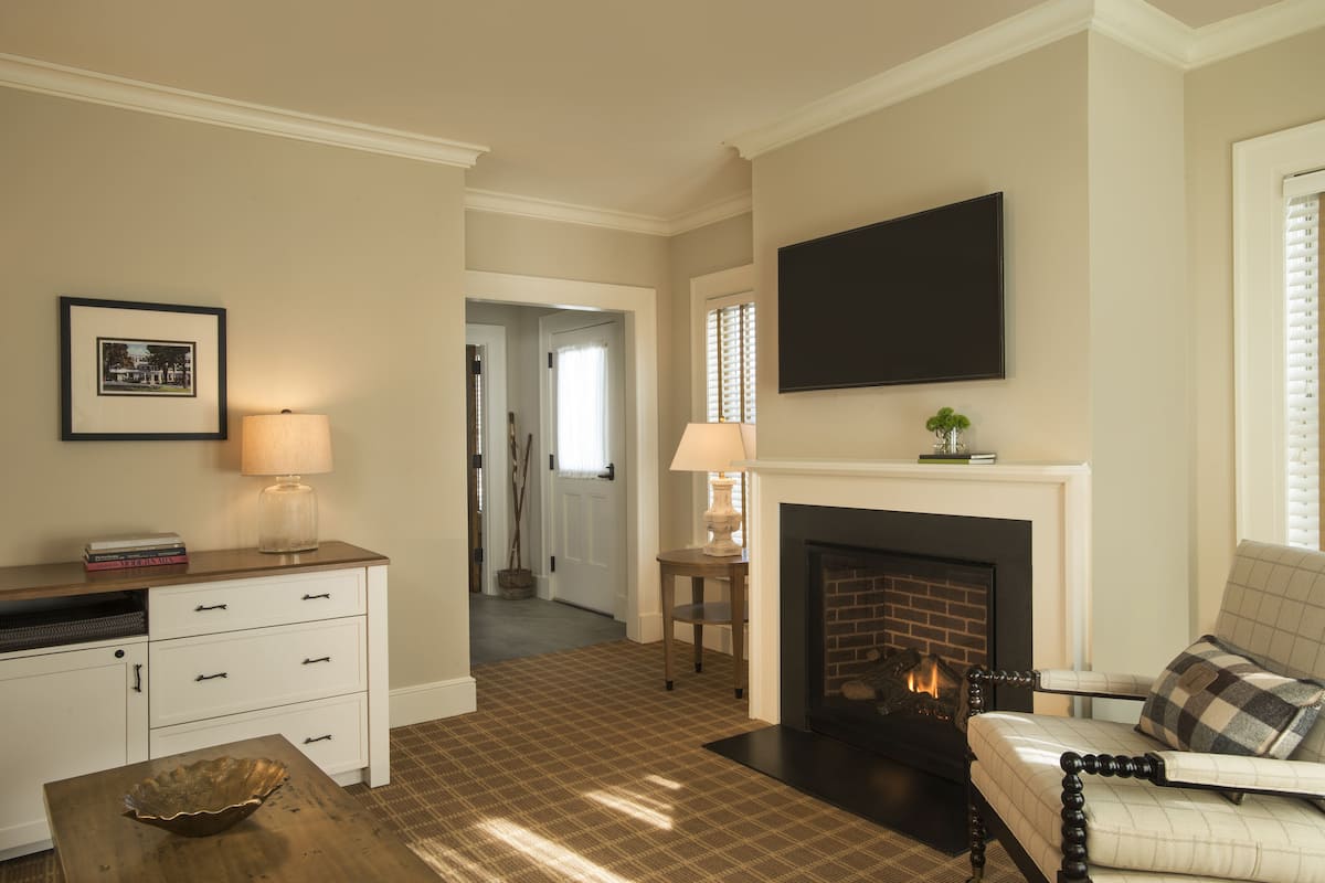 A living room with a fireplace, a television mounted above it, a sofa, a coffee table, and a sideboard with drawers.