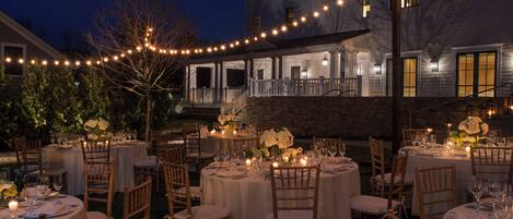 An outdoor dining area with round tables, chairs, and string lights.