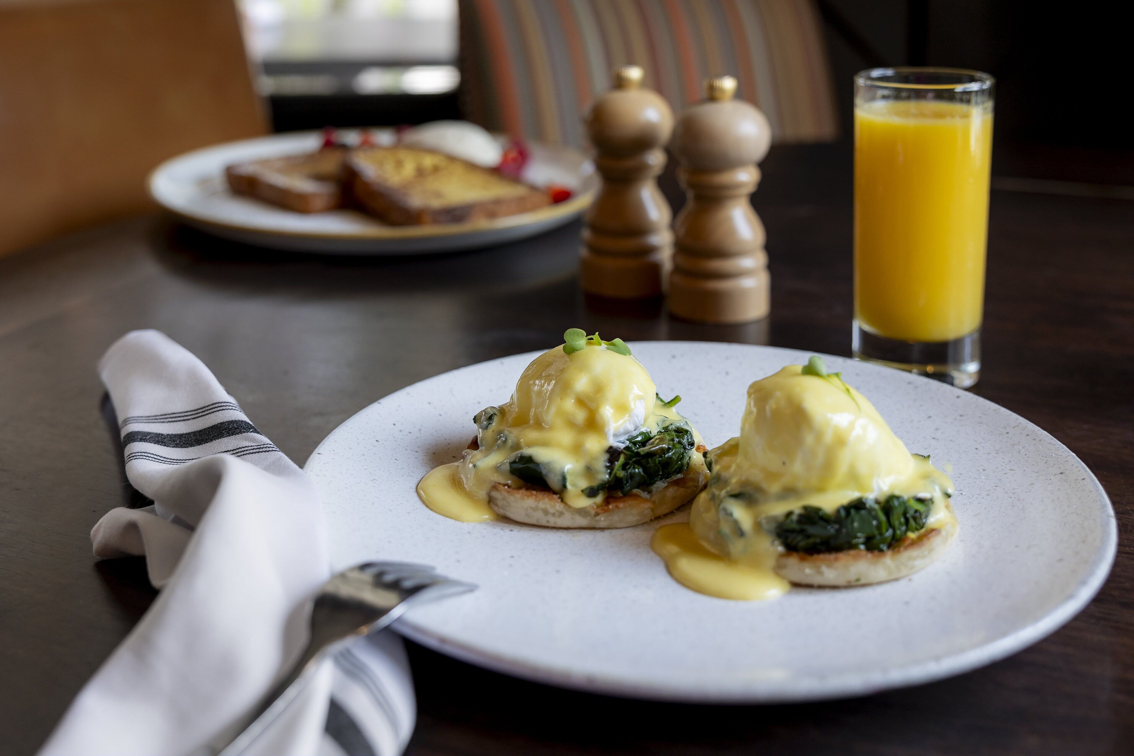 A breakfast setting with eggs benedict on a plate, toast, a glass of orange juice, and a napkin.