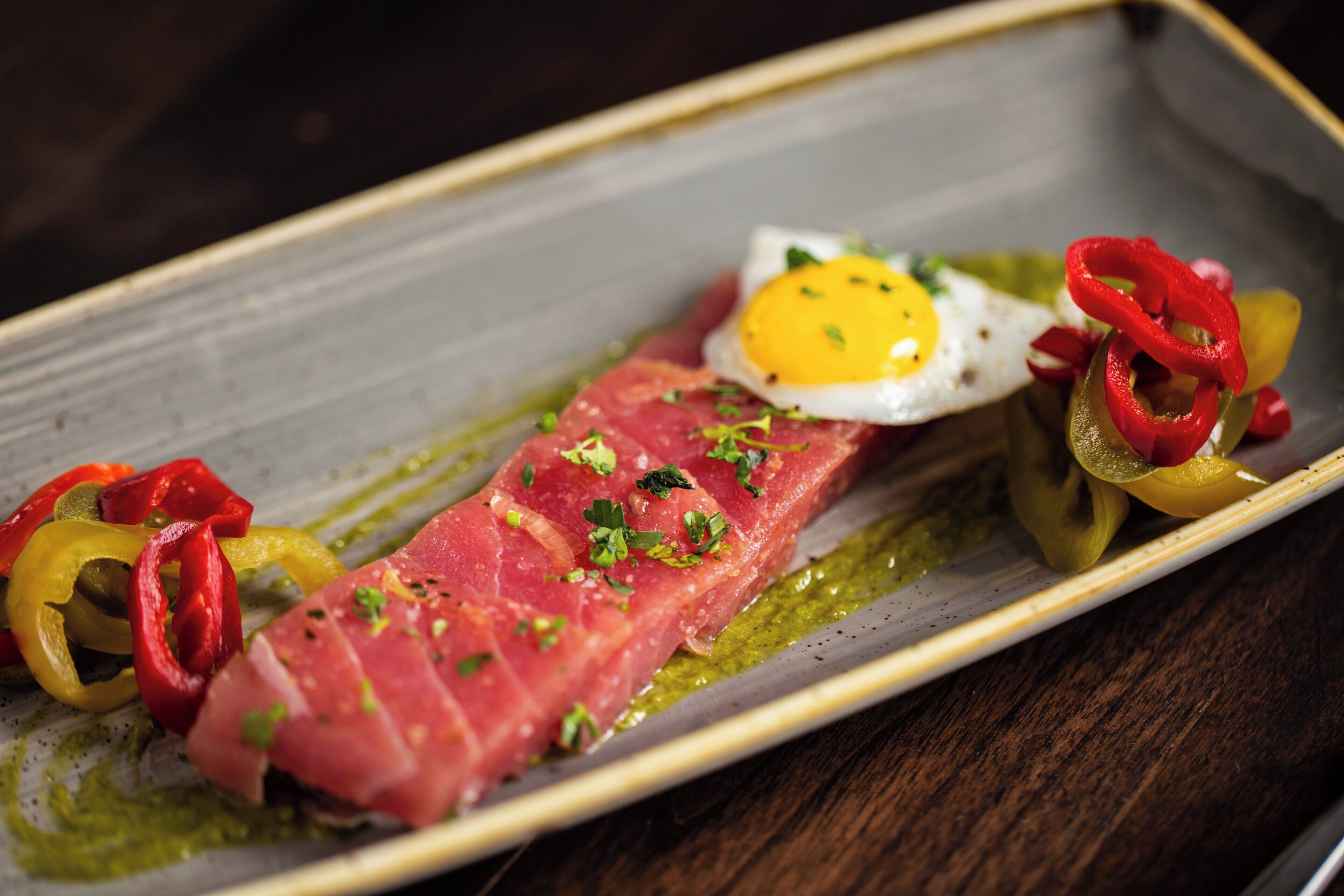 A dish with a slice of meat, a fried egg, and sliced peppers on a plate.