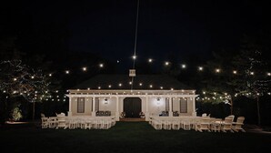 A white building with a covered entrance, surrounded by white chairs arranged in rows, and string lights overhead. - Kimpton Taconic Hotel by IHG (Manchester)